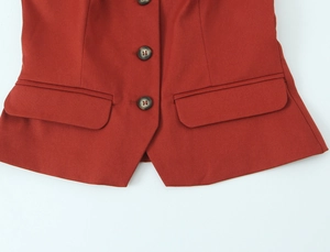Detail shot of brick red vest featuring three brown buttons and symmetrical flap pockets