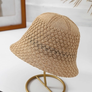 Detail shot of beige knitted bucket hat with hollow-out design on a gold stand.
