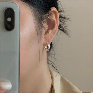 Close-up of minimalist silver twisted hoop earrings worn on ear with casual styling