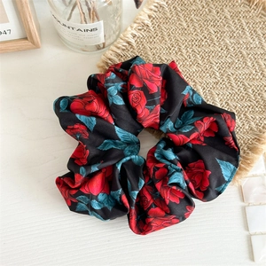 Detailed close-up of a floral scrunchie with red roses and green leaves on black silk