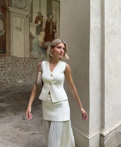 Photo street style d'un ensemble de gilet en tricot blanc cassé avec jupe plissée et mur mural