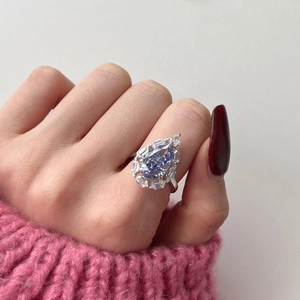 Close-up of a pear-shaped blue gemstone ring with baguette diamond accents on a finger