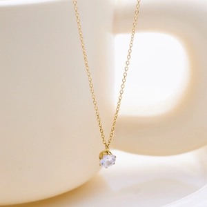 Detail of a minimalist gold necklace with a round solitaire zircon pendant on a ceramic cup
