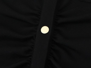 Détail d'une robe en crêpe noir avec fronces et bouton en métal doré poli
