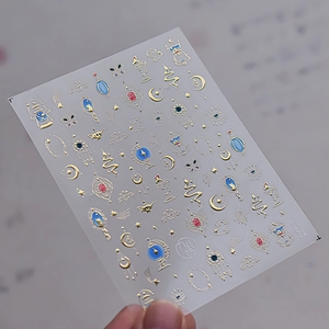 Makroaufnahme von Goldfolien-Nagelstickern mit Sternen, Mond und mystischen Alchemie-Motiven