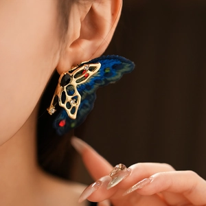 Détail d'une boucle d'oreille papillon vintage avec métal doré, pierres et broderie bleue