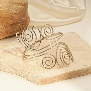 Macro detail of golden spiral cuff bracelet on white stone and satin background
