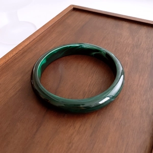 Detail view of deep green marble acrylic bangle on rustic dark brown wooden tray