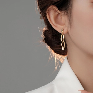 Close-up of a gold irregular lava wave earring on a model with elegant side lighting