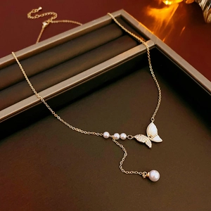 Gros plan d'un collier en Y doré avec papillon en nacre et perles sur présentoir bijoux