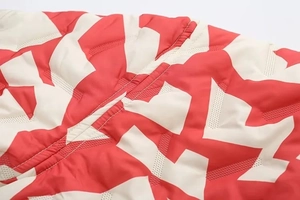 Gros plan du motif géométrique rouge et beige sur veste matelassée avec coutures