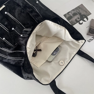 Detail of black velvet tote bag with white pearl accents and magnetic closure interior