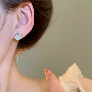 Macro side view of cute silver rabbit stud earrings with clear zircon stones on earlobe