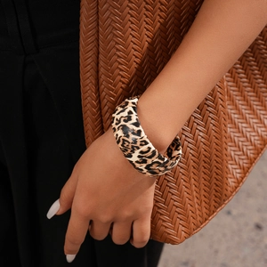 Detail showing stylish leopard print acrylic wide bangle worn with a chic brown outfit