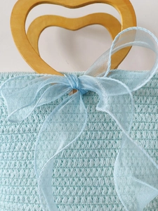 Light blue woven handbag with gold heart-shaped handle and sheer bow decoration