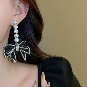 Close-up of dangling black bow earrings with sparkling zircons worn by a model