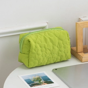 Close-up of green quilted makeup bag with floral stitching on a white table