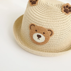 Close-up of children's woven straw hat featuring cute bear patch and ear decorations