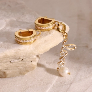 Detailed macro shot of gold stainless steel zircon earrings with Love pendant and white pearl