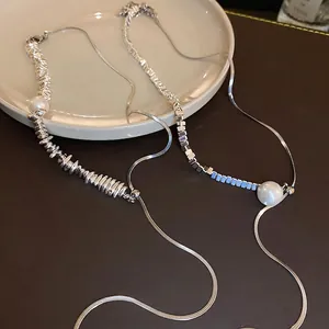 Asymmetric silver snake chain necklace with white pearls and blue beads on a tray