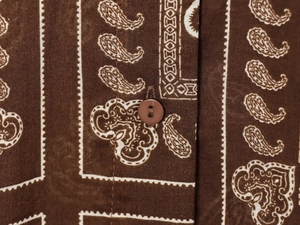 Macro detail of paisley print fabric and matching round button on a brown summer shirt