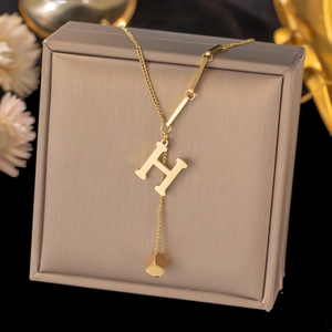 Detail of gold titanium steel H-letter pendant necklace with square charm on jewelry box