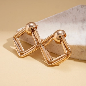 Close-up of gold geometric square interlocking earrings on a natural stone base