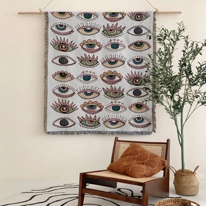 Bohemian evil eye woven blanket with fringes hanging on a minimalist wooden rack