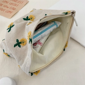 Détail de la broderie marguerite sur une trousse de maquillage en toile crème avec zip