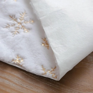 Close-up of white plush table runner featuring gold sequin snowflake patterns on wood