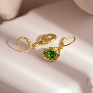 Detail of vintage gold earrings with emerald green stones and diamond halo accents