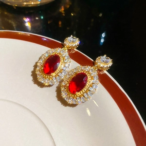 Macro detail of oval gold plated earrings with ruby red stones and white zircon stones