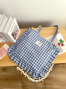 Detail of blue plaid tote bag with ruffle edges on a wooden surface with props