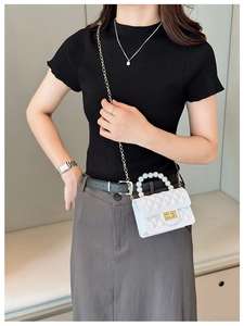 Detail of white quilted crossbody bag with pearl handle and golden chain strap
