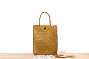 Detail of a handmade straw tote bag on a wooden table with a teacup and dry flowers