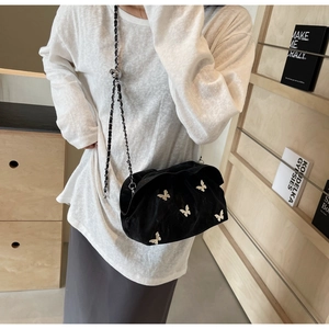 Detail of black pleated bucket bag with silver butterfly charm and woven chain strap