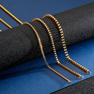 Detailed view of three gold stainless steel box chains on a textured cylinder