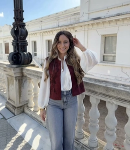 Detail of dark red embroidered velvet vest layered over a white shirt in a classic balcony setting