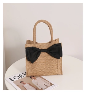 Detailed close-up of a beige straw handbag with a large black fabric bow and woven handle