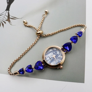 Close-up of golden bracelet watch with blue heart-shaped stones and pearl dial