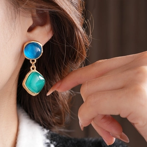 Détail de boucles d'oreilles vintage dorées avec pierres bleue et verte sur un mannequin