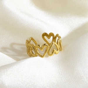 Detail of gold-plated stainless steel ring with hollow heart design on white silk fabric