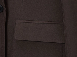 Détail d'un blazer marron foncé avec poche à rabat et bouton noir en gros plan