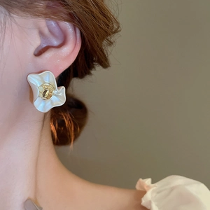 Macro shot of French style white wrinkled flower earring with gold textured center on ear