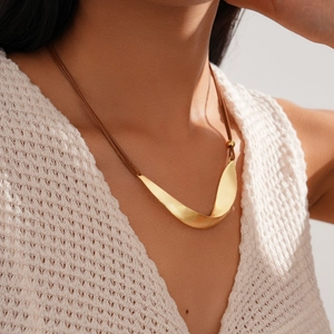 Close-up of twisted gold brushed metal ribbon pendant on a brown cord necklace