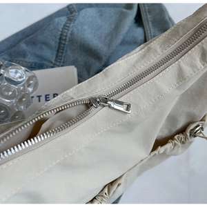 Detail of high-quality silver metal zipper on light beige pleated nylon crossbody bag