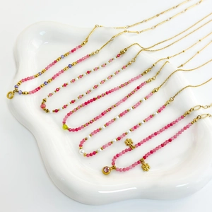 Detail view of 18K gold-plated beaded necklaces with colorful stones on a ceramic tray