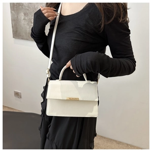 Detailed view of cream-white patent leather bag with elegant gold metal buckle and stitching