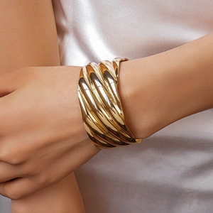 Detailed close-up of wide golden cuff bracelet featuring elegant wavy spiral texture