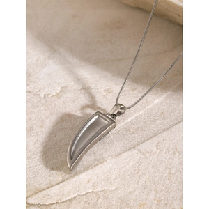 Detailed close-up of a silver-toned tusk pendant on a fine chain over stone